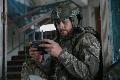 Photo of Military mission. Soldier in uniform with drone controller inside abandoned building