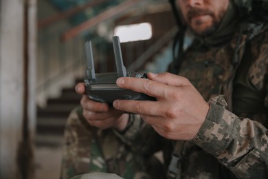 Military mission. Soldier in uniform with drone controller inside abandoned building, closeup