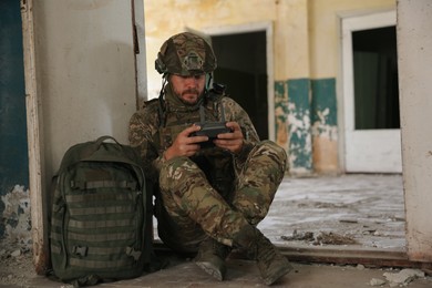 Photo of Military mission. Soldier in uniform with drone controller inside abandoned building