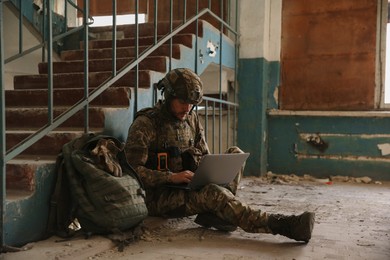 Photo of Military mission. Soldier in uniform using laptop inside abandoned building