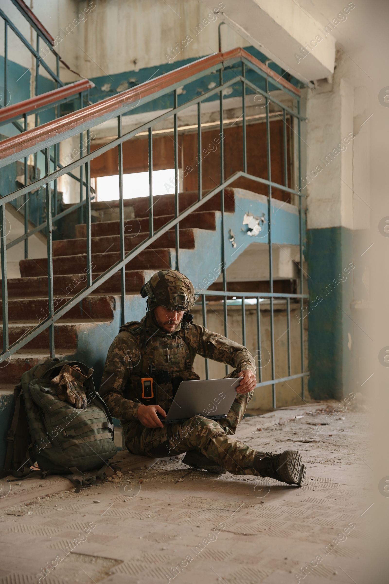 Photo of Military mission. Soldier in uniform using laptop inside abandoned building