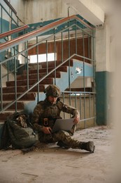 Military mission. Soldier in uniform using laptop inside abandoned building