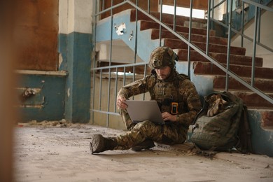 Photo of Military mission. Soldier in uniform using laptop inside abandoned building