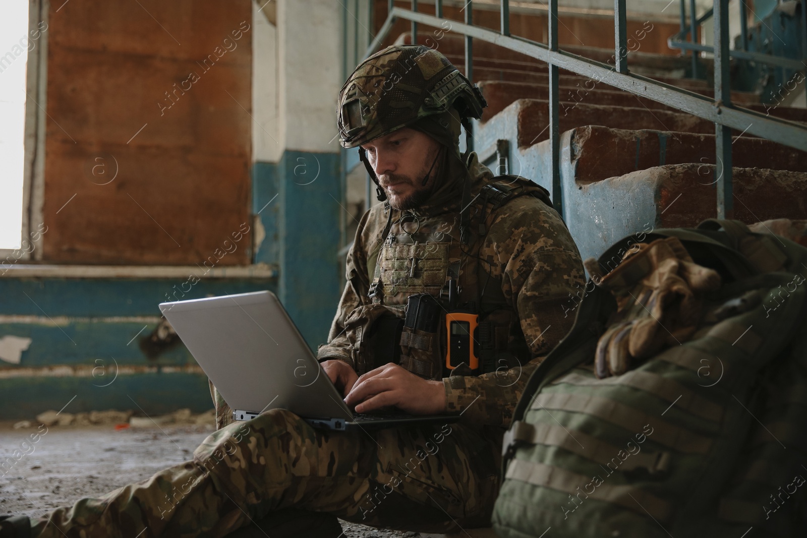 Photo of Military mission. Soldier in uniform using laptop inside abandoned building