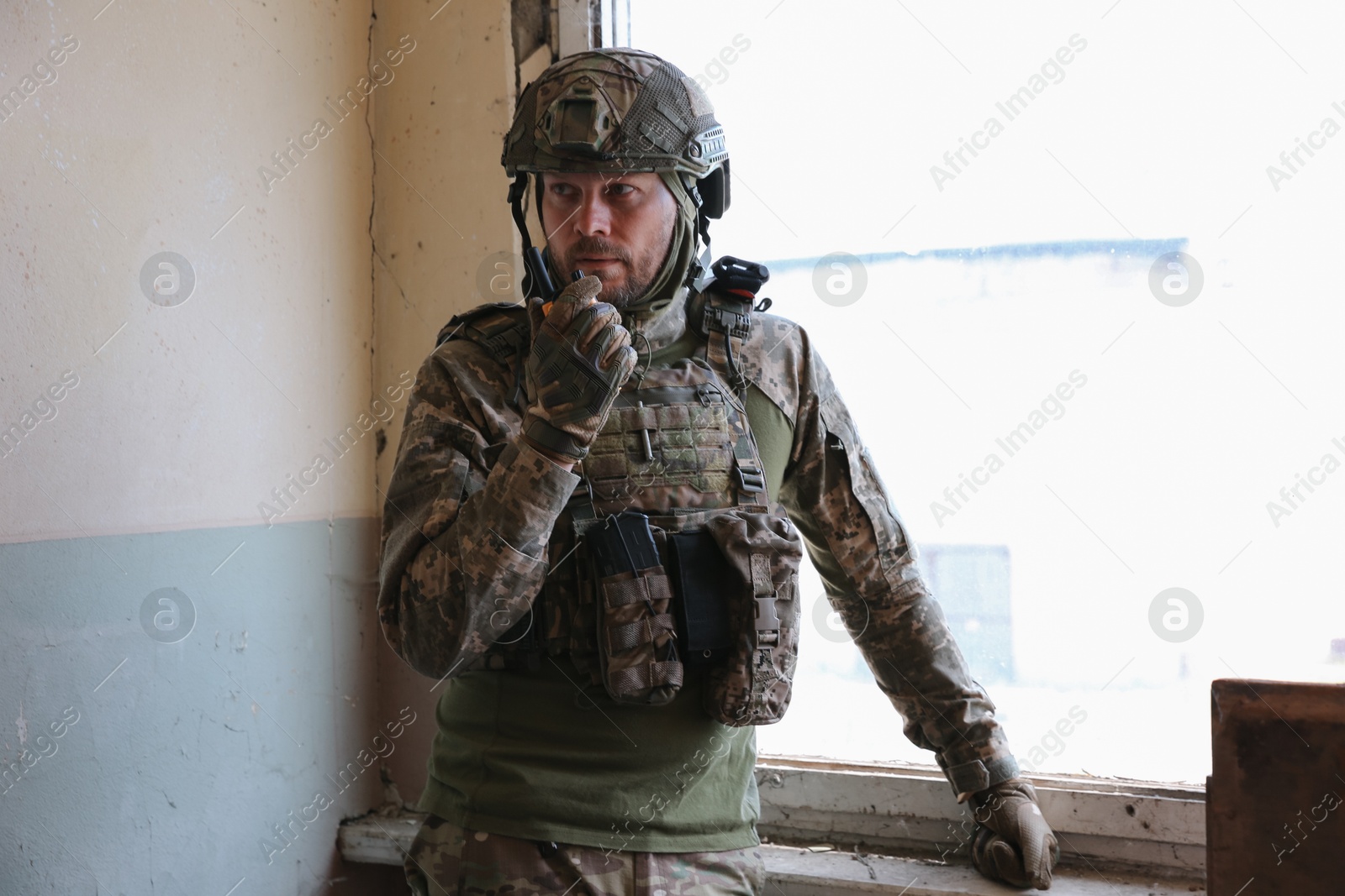 Photo of Military mission. Soldier in uniform with radio transmitter inside abandoned building