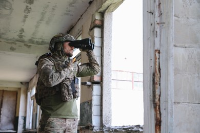 Military mission. Soldier in uniform with binoculars inside abandoned building, space for text