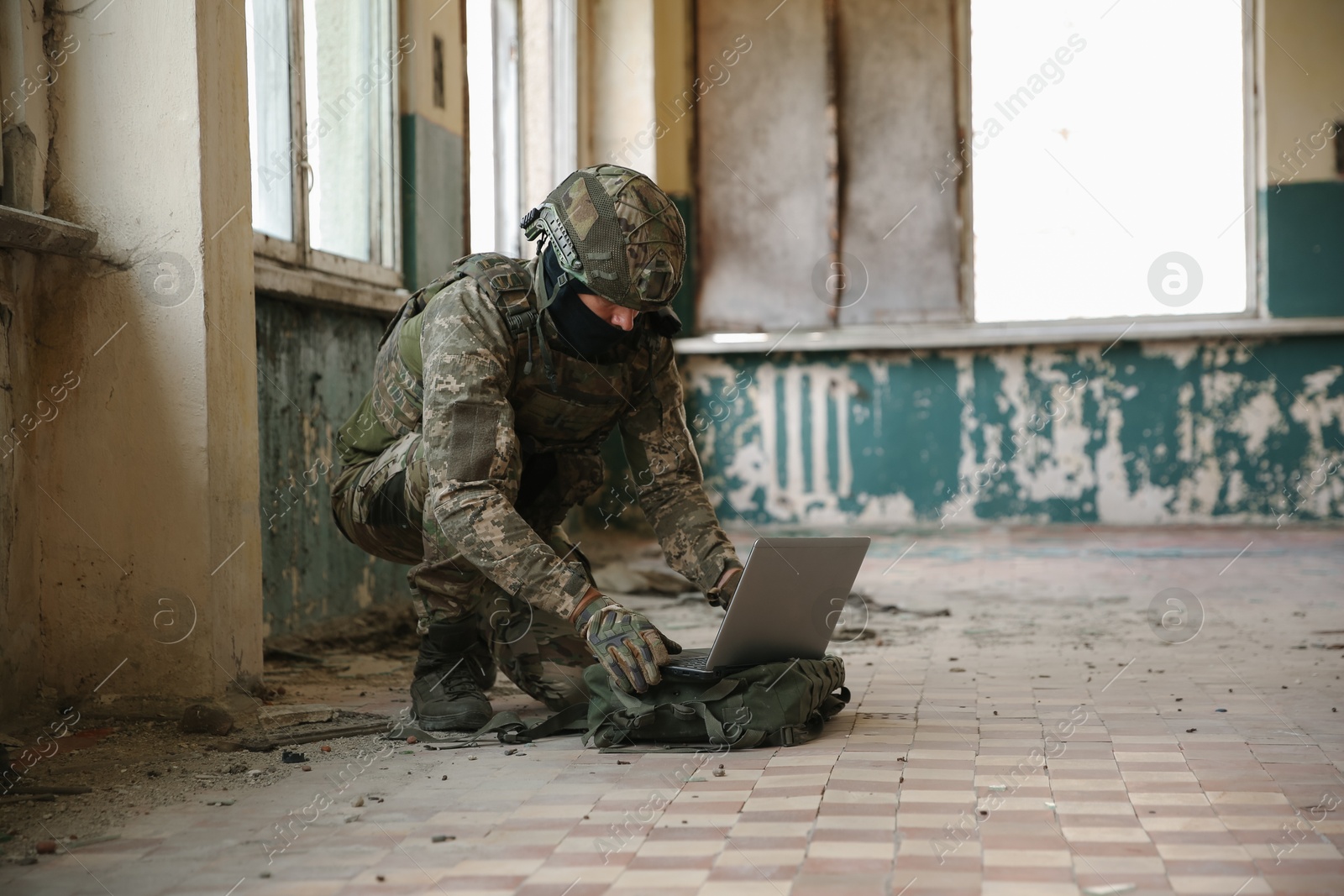 Photo of Military mission. Soldier in uniform using laptop inside abandoned building, space for text