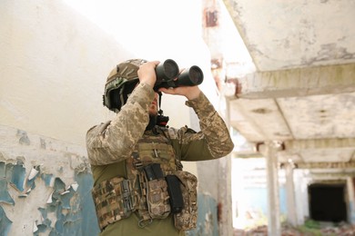 Photo of Military mission. Soldier in uniform with binoculars inside abandoned building