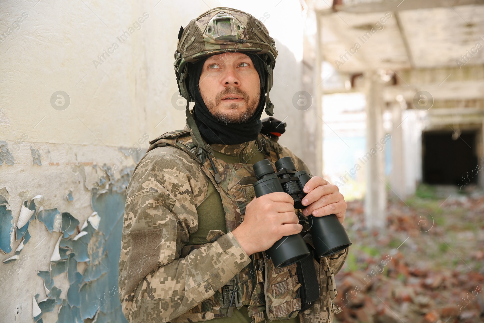 Photo of Military mission. Soldier in uniform with binoculars inside abandoned building