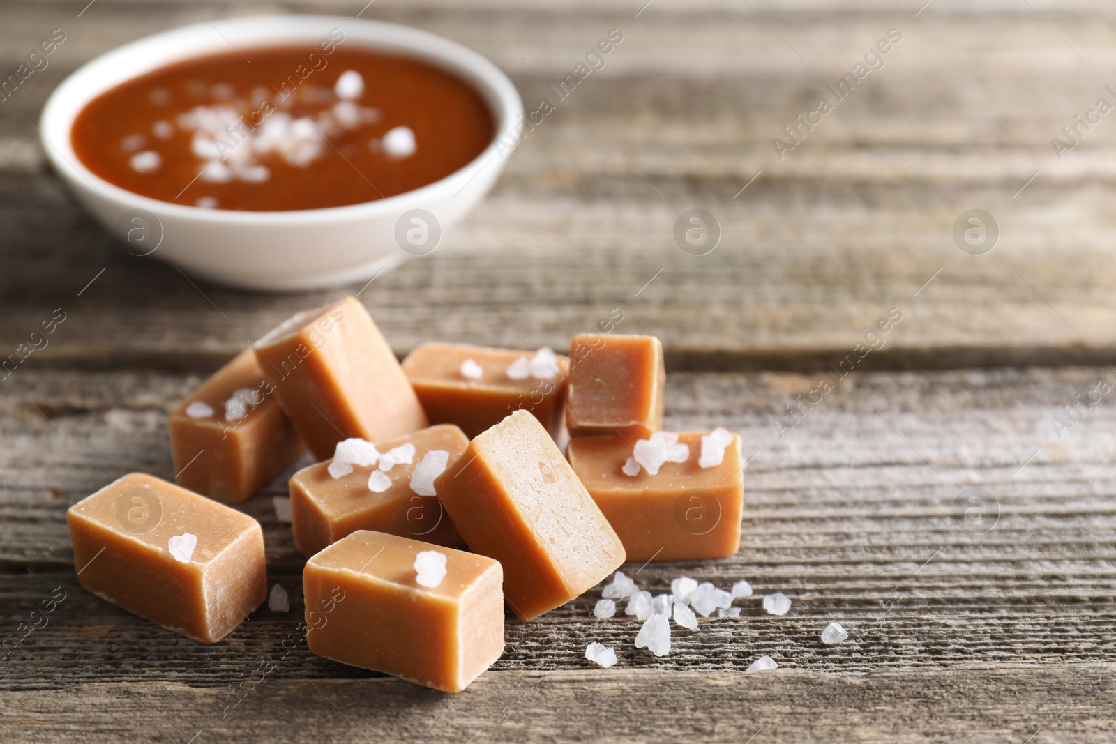 Photo of Yummy caramel candies with sea salt on wooden table, closeup