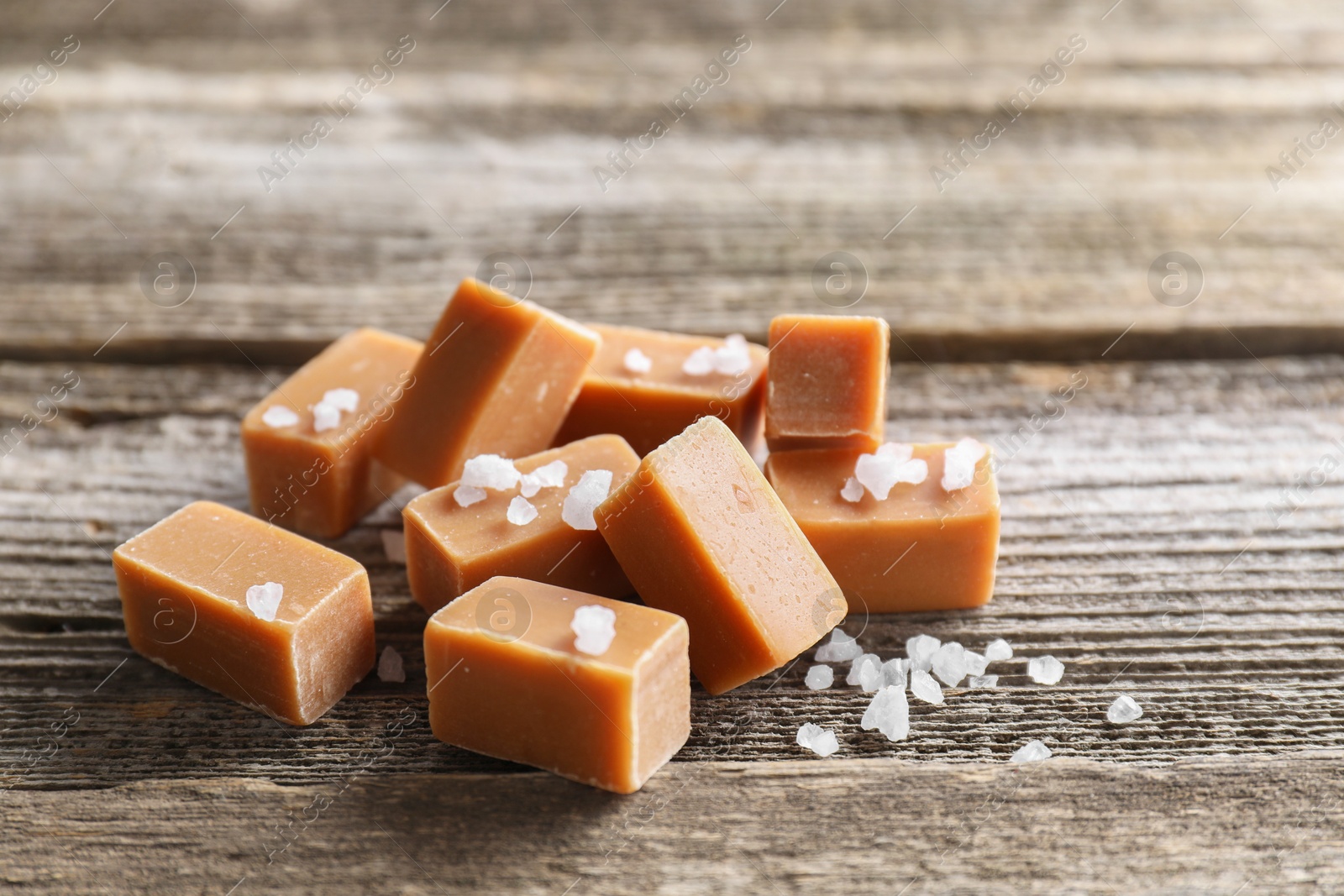 Photo of Yummy caramel candies with sea salt on wooden table, closeup