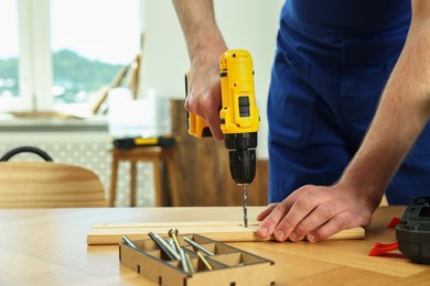 Photo of Craftsman working with drill at wooden table in workshop, closeup