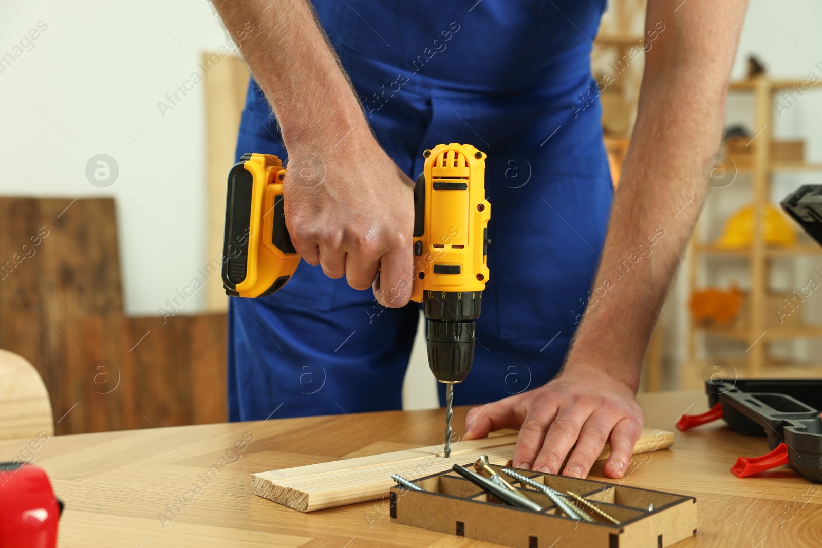 Photo of Craftsman working with drill at wooden table in workshop, closeup