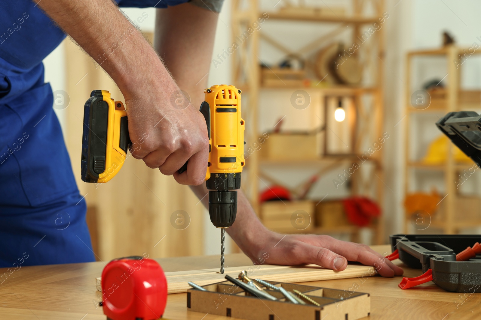 Photo of Craftsman working with drill at wooden table in workshop, closeup