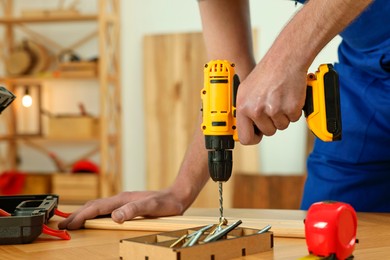 Craftsman working with drill at wooden table in workshop, closeup