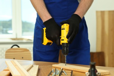 Photo of Craftsman working with drill at wooden table in workshop, closeup