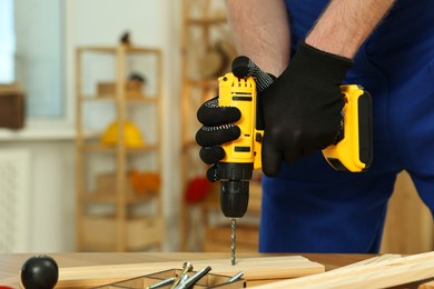 Craftsman working with drill at wooden table in workshop, closeup. Space for text