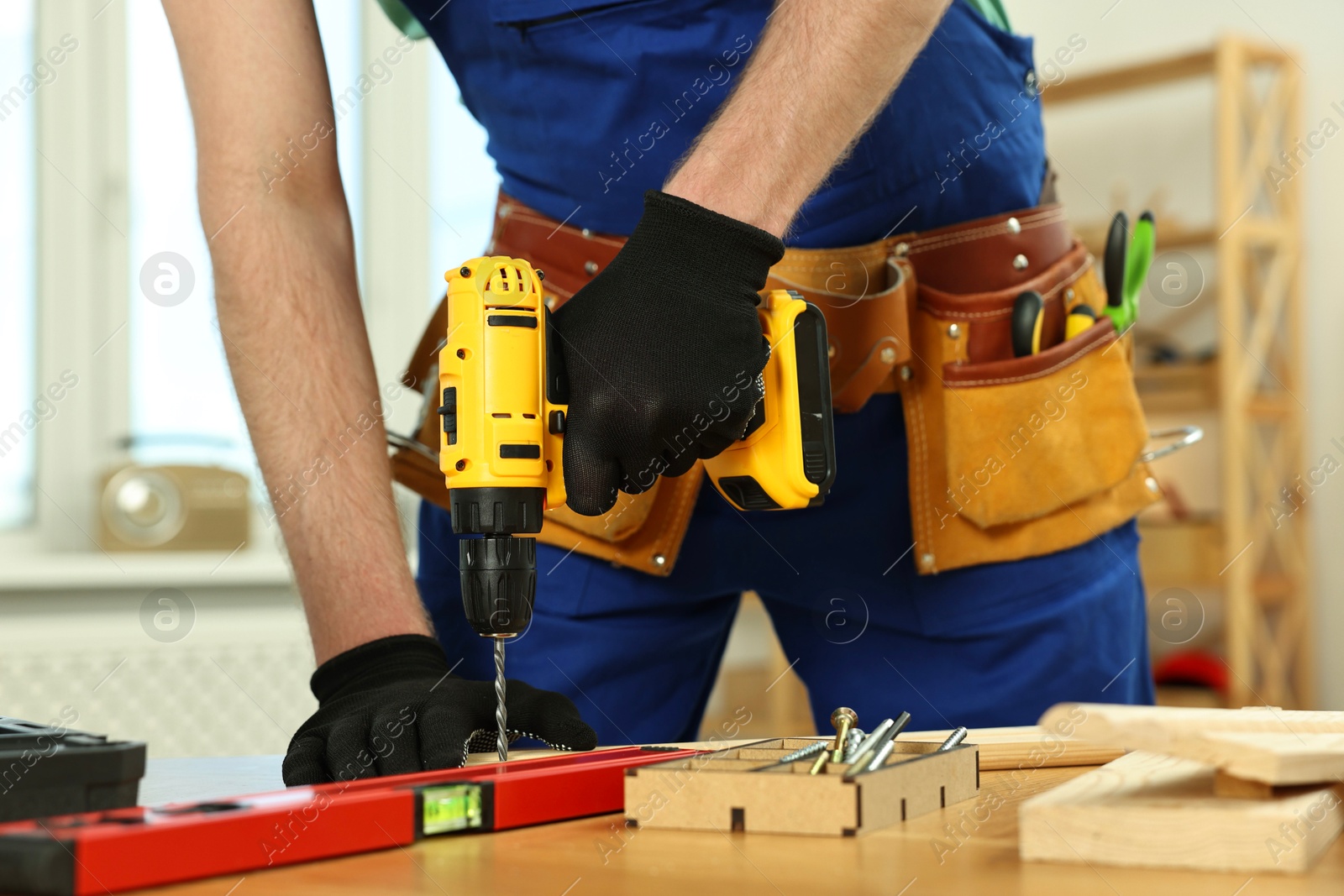 Photo of Craftsman working with drill at wooden table in workshop, closeup