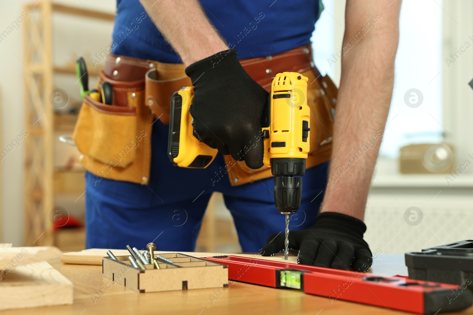 Photo of Craftsman working with drill at wooden table in workshop, closeup