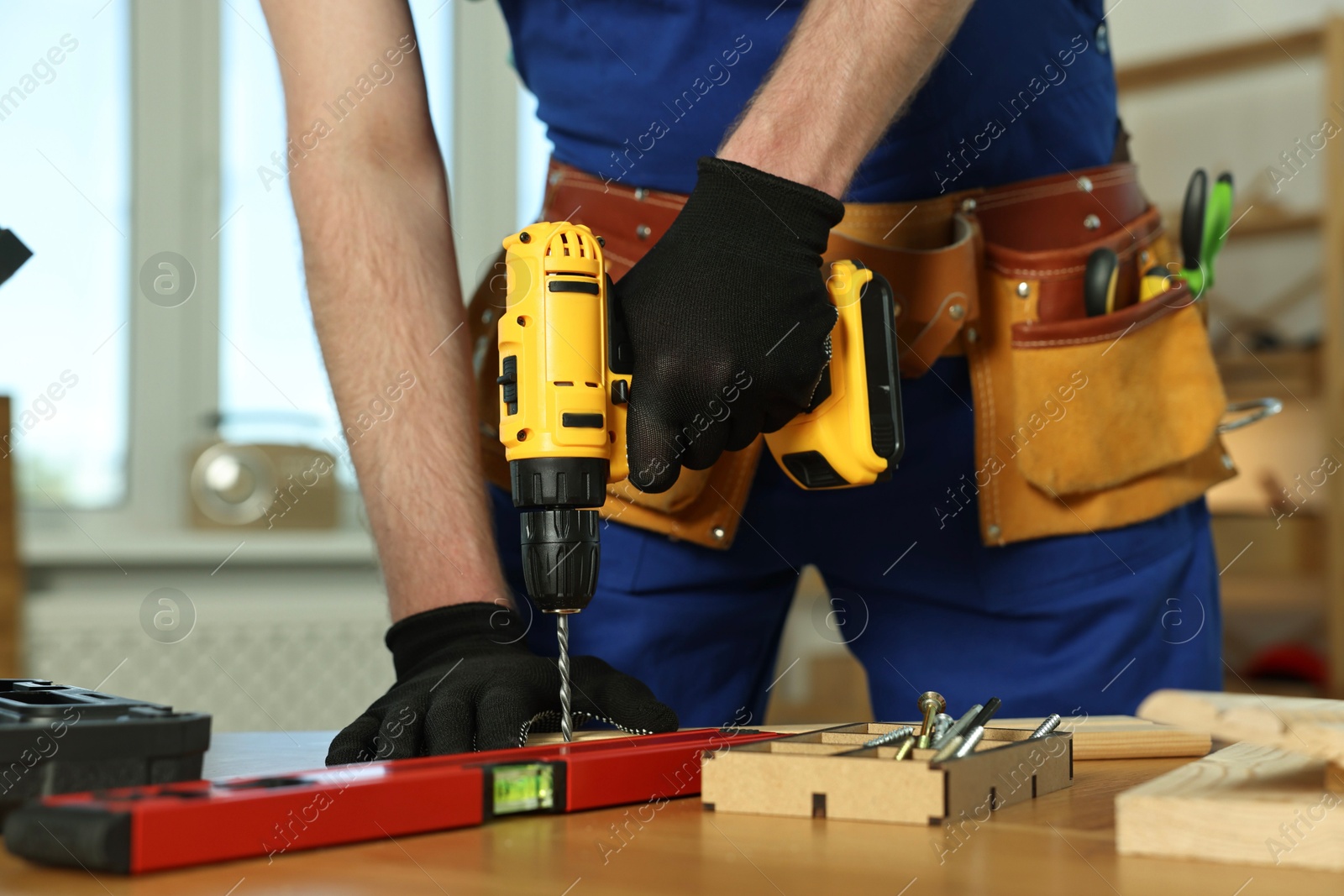 Photo of Craftsman working with drill at wooden table in workshop, closeup