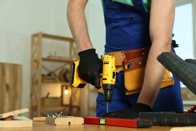 Photo of Craftsman working with drill at wooden table in workshop, closeup. Space for text