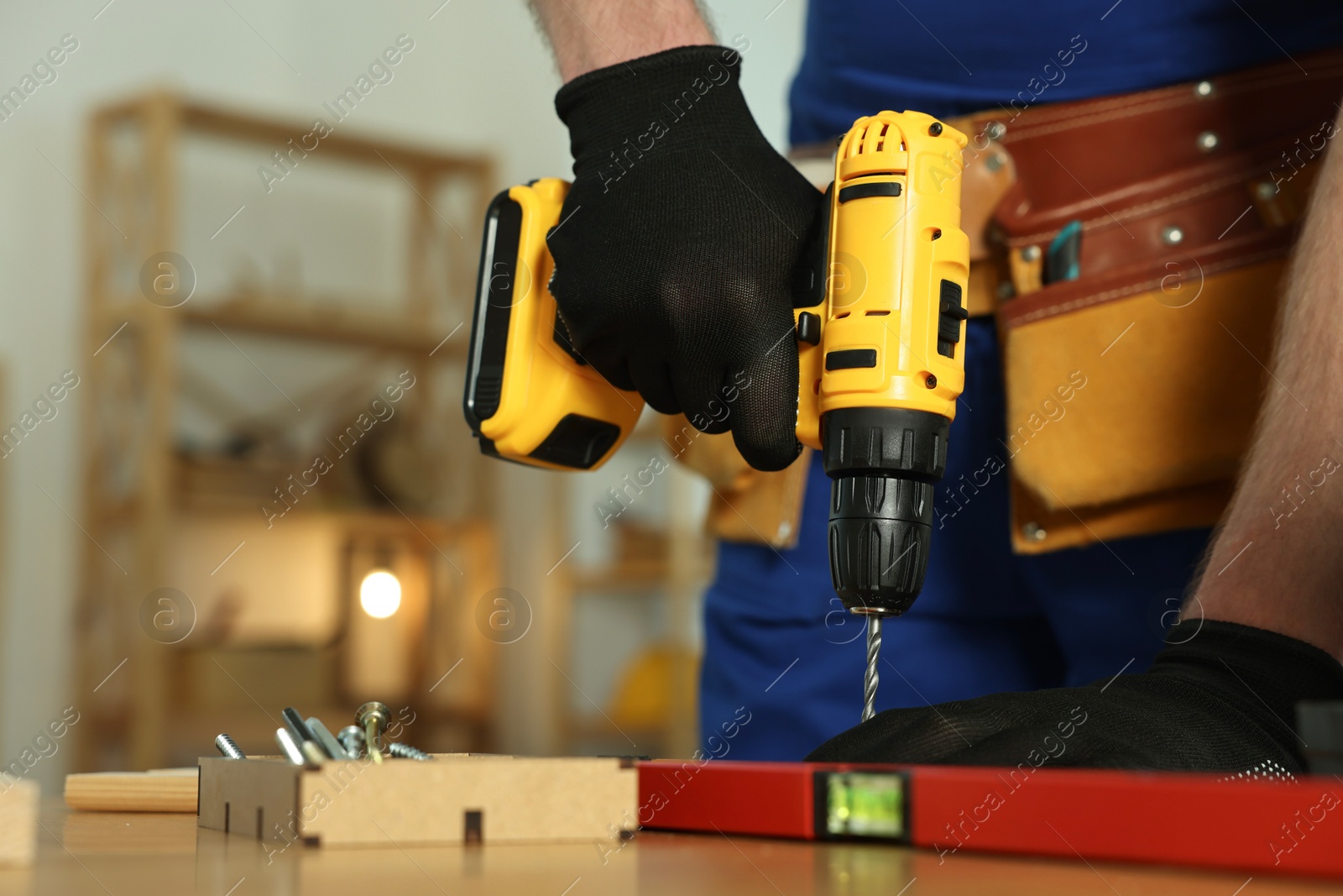 Photo of Craftsman working with drill at wooden table in workshop, closeup