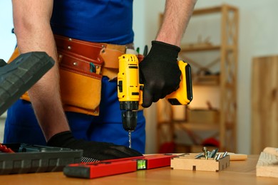 Craftsman working with drill at wooden table in workshop, closeup