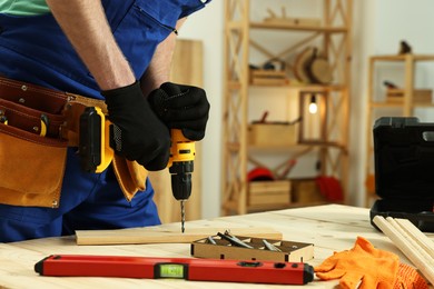 Photo of Craftsman working with drill at wooden table in workshop, closeup. Space for text