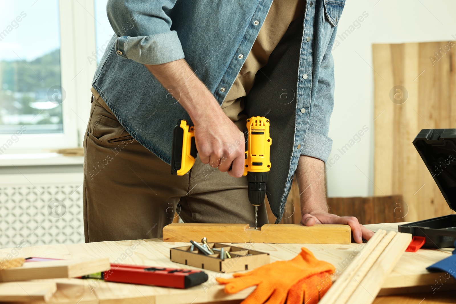 Photo of Craftsman working with drill at wooden table in workshop, closeup