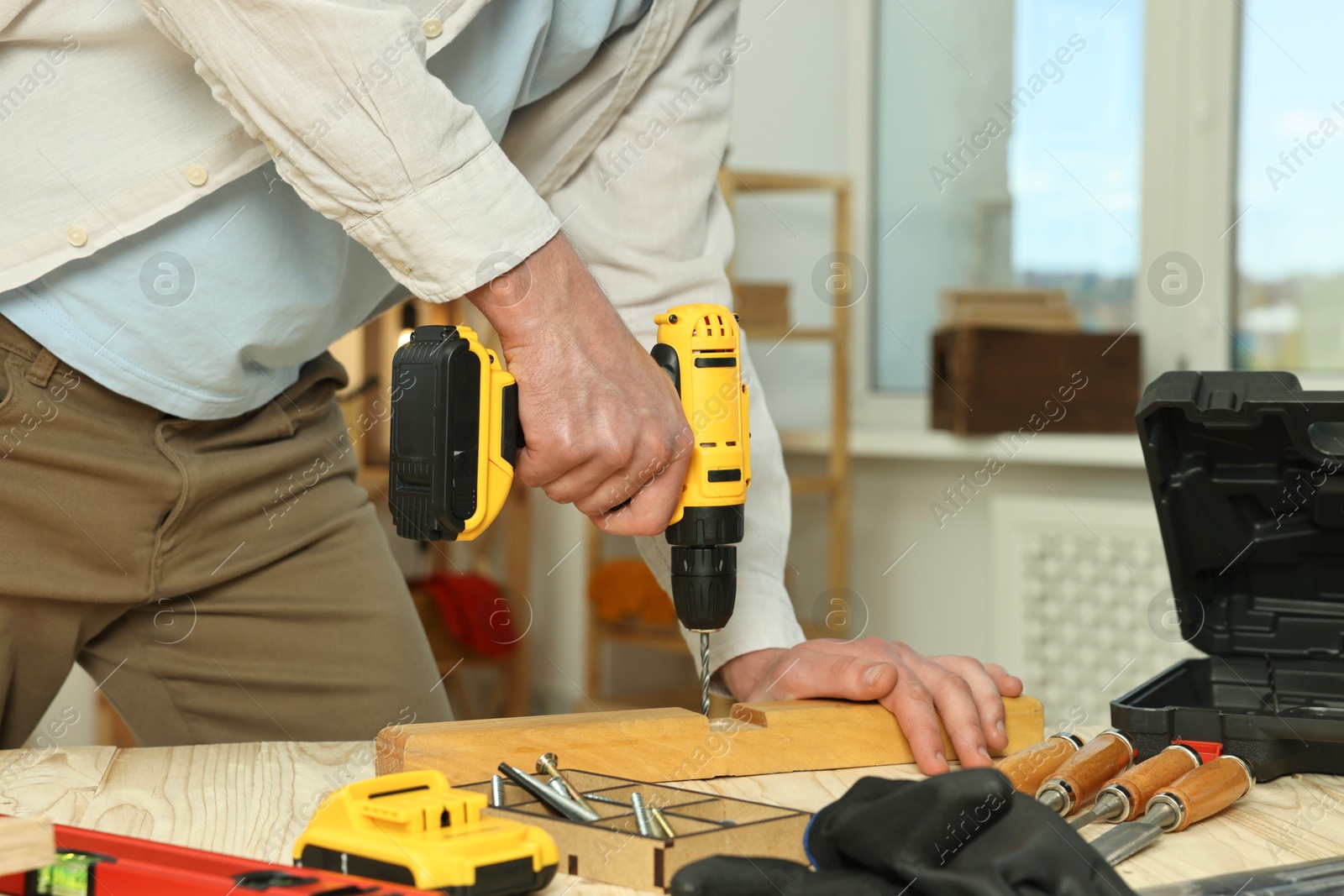 Photo of Craftsman working with drill at wooden table in workshop, closeup