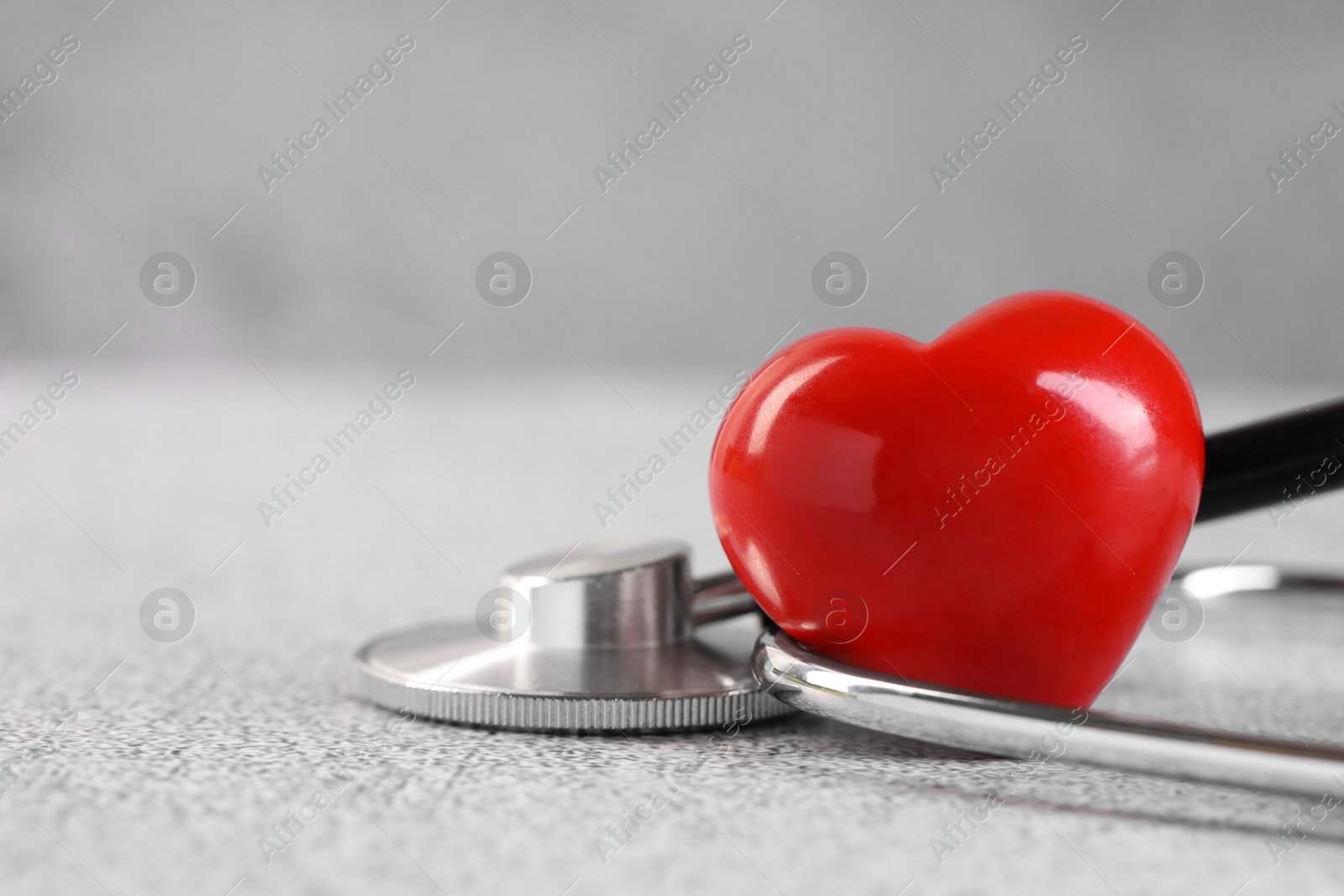 Photo of Stethoscope and red heart on grey stone table. Space for text