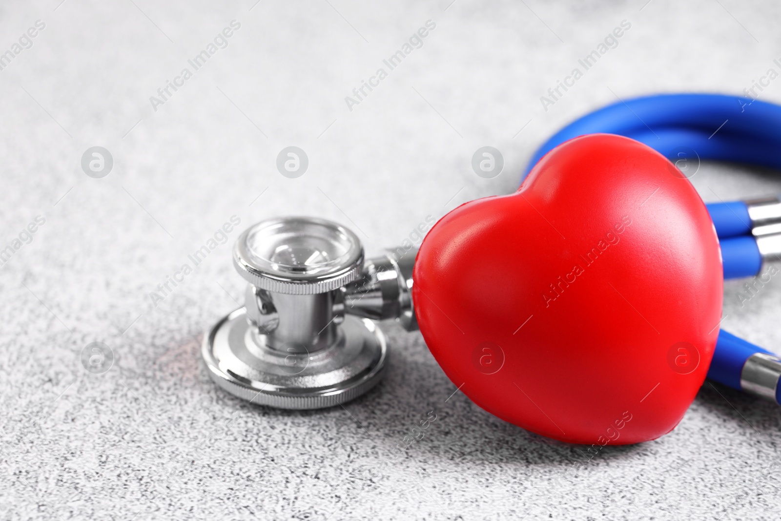 Photo of Stethoscope and red heart on grey stone table, closeup