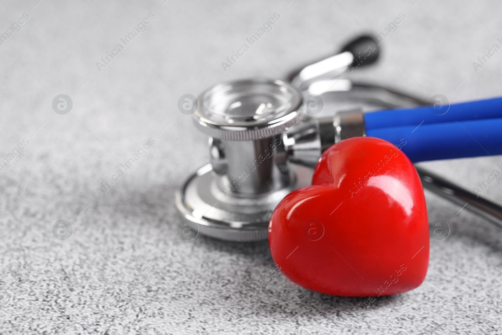 Photo of Stethoscope and red heart on grey stone table. Space for text