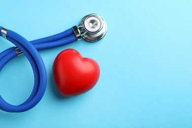 Photo of Stethoscope and red heart on light blue background, top view. Space for text