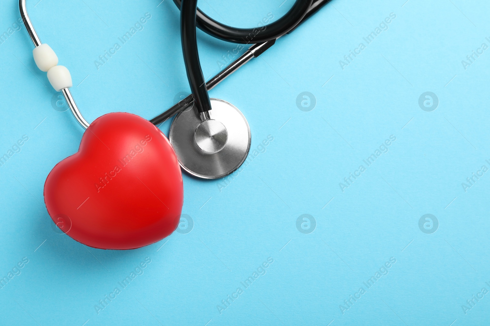 Photo of Stethoscope and red heart on light blue background, top view. Space for text