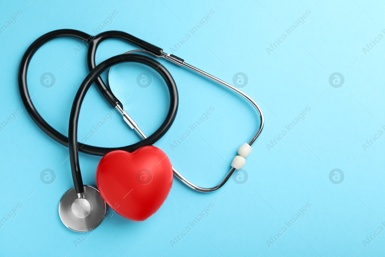 Photo of Stethoscope and red heart on light blue background, top view. Space for text