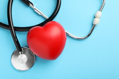 Stethoscope and red heart on light blue background, top view