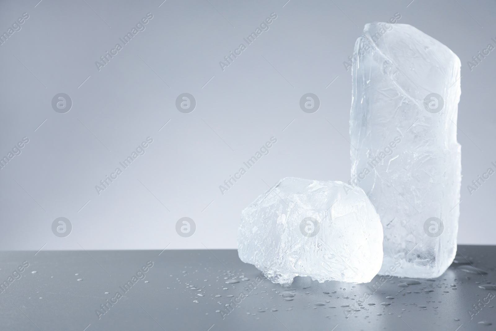 Photo of Pieces of clear ice and water drops on light grey table. Space for text