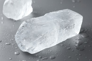 Photo of Pieces of clear ice and water drops on light grey table, closeup