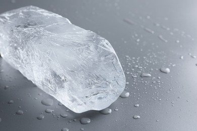 Photo of Piece of clear ice and water drops on light grey table, closeup. Space for text