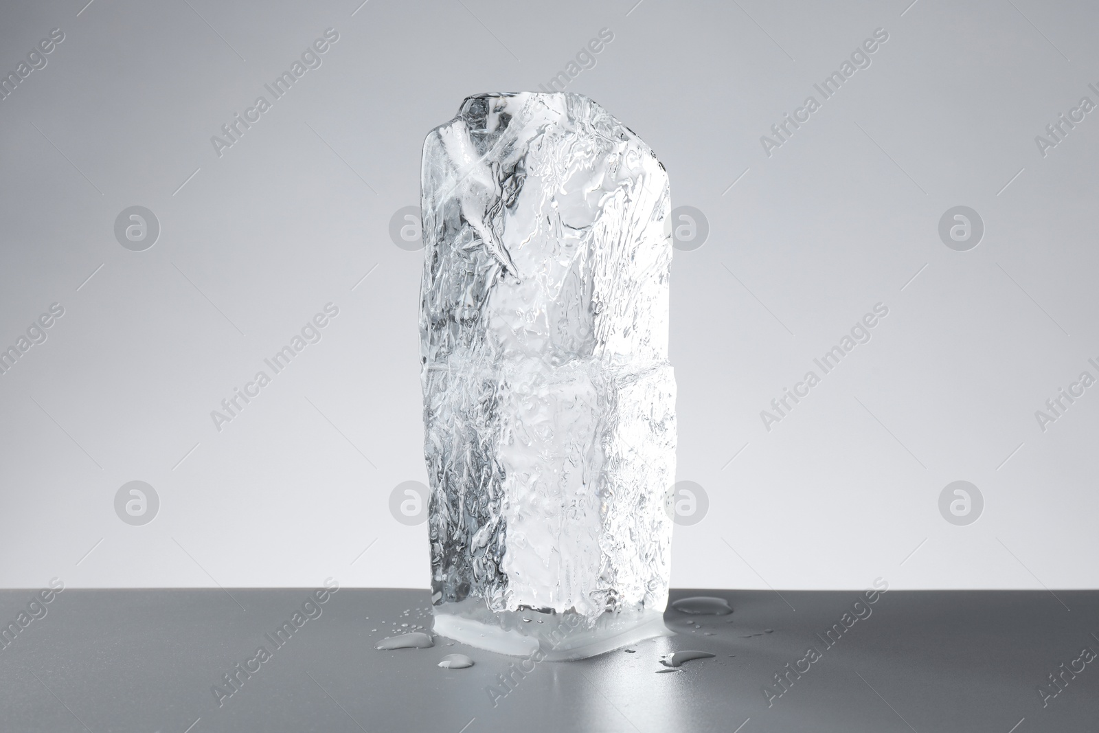 Photo of Piece of clear ice and water drops on light grey table