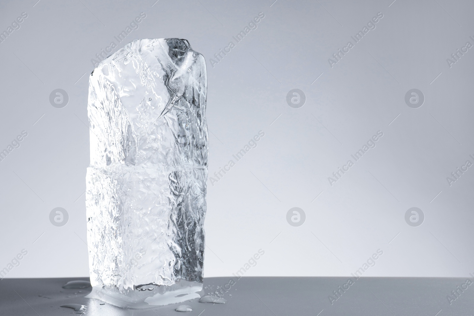 Photo of Piece of clear ice and water drops on light grey table. Space for text