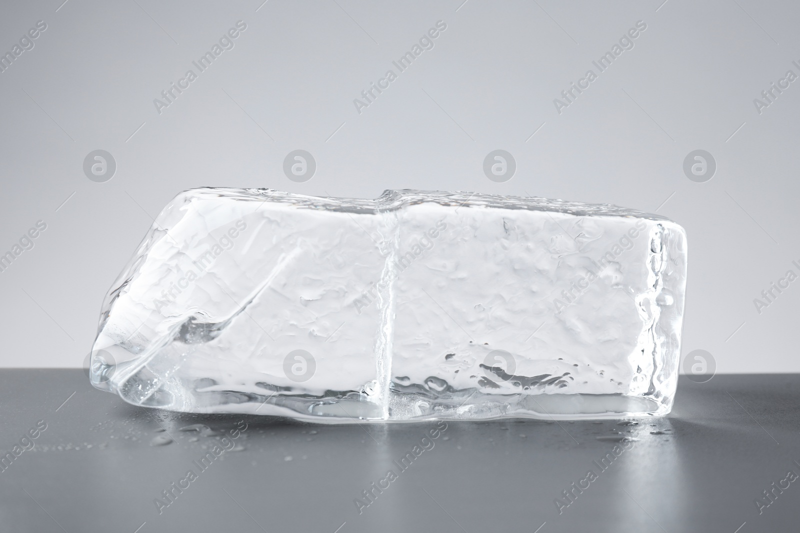 Photo of Piece of clear ice and water drops on light grey table