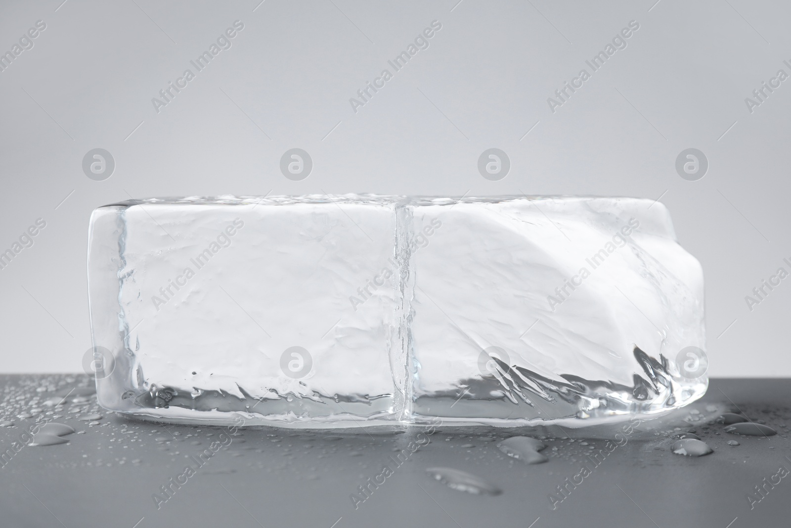 Photo of Piece of clear ice and water drops on light grey table