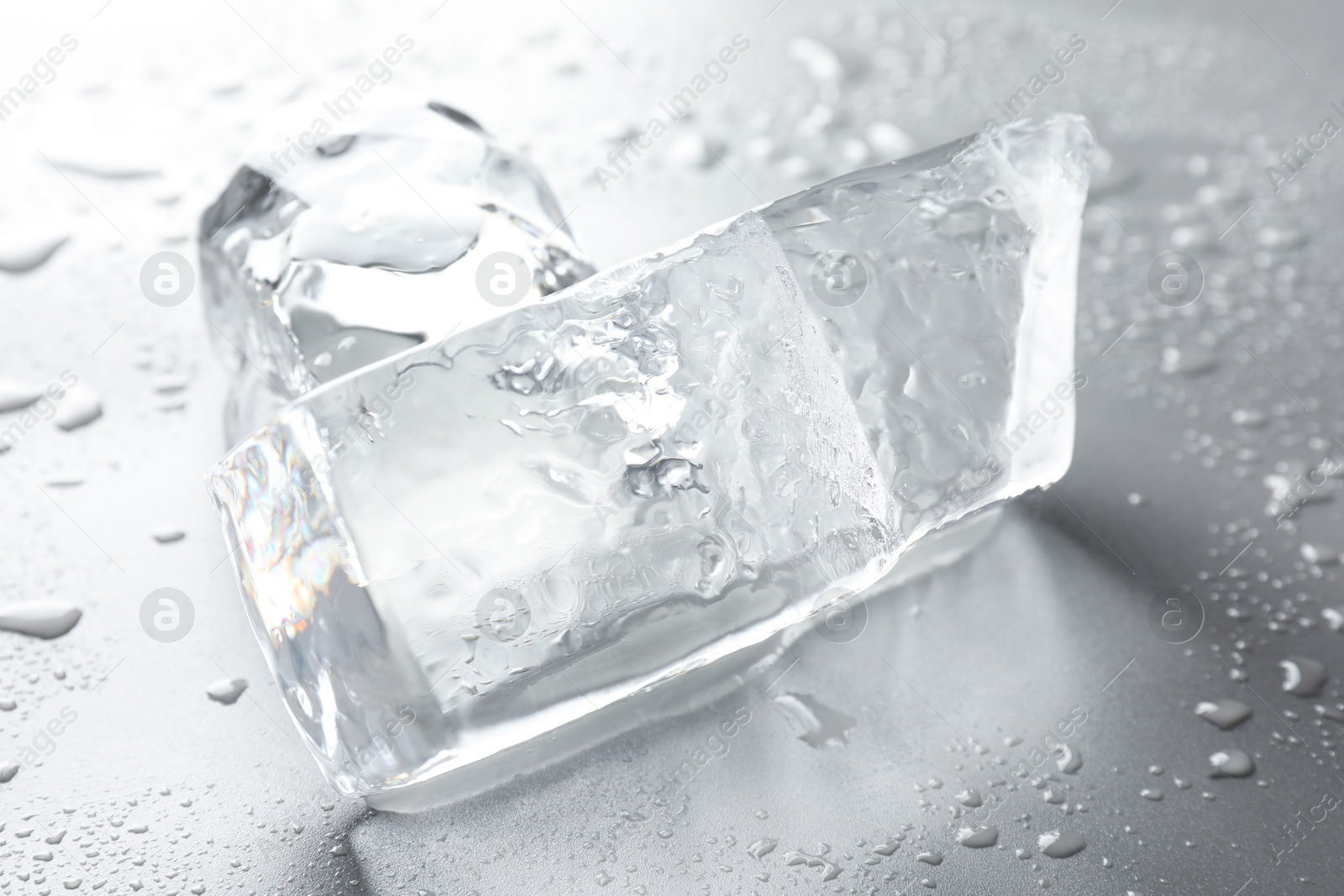 Photo of Pieces of clear ice and water drops on light grey table