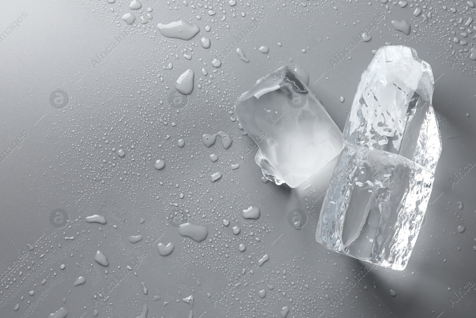 Photo of Pieces of clear ice and water drops on light grey table, top view. Space for text