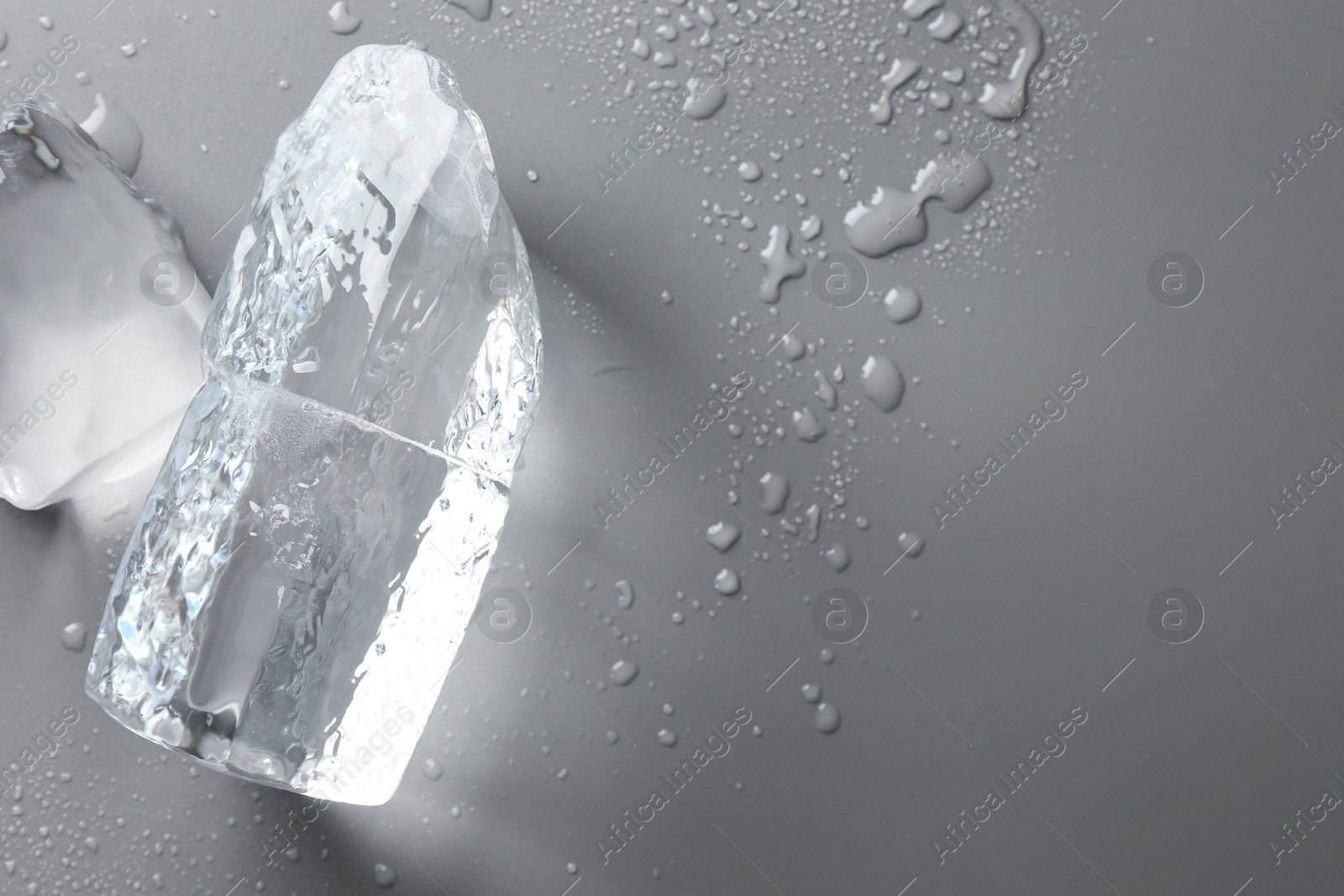 Photo of Pieces of clear ice and water drops on light grey table, top view. Space for text