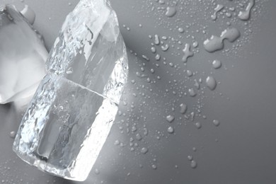 Pieces of clear ice and water drops on light grey table, top view. Space for text