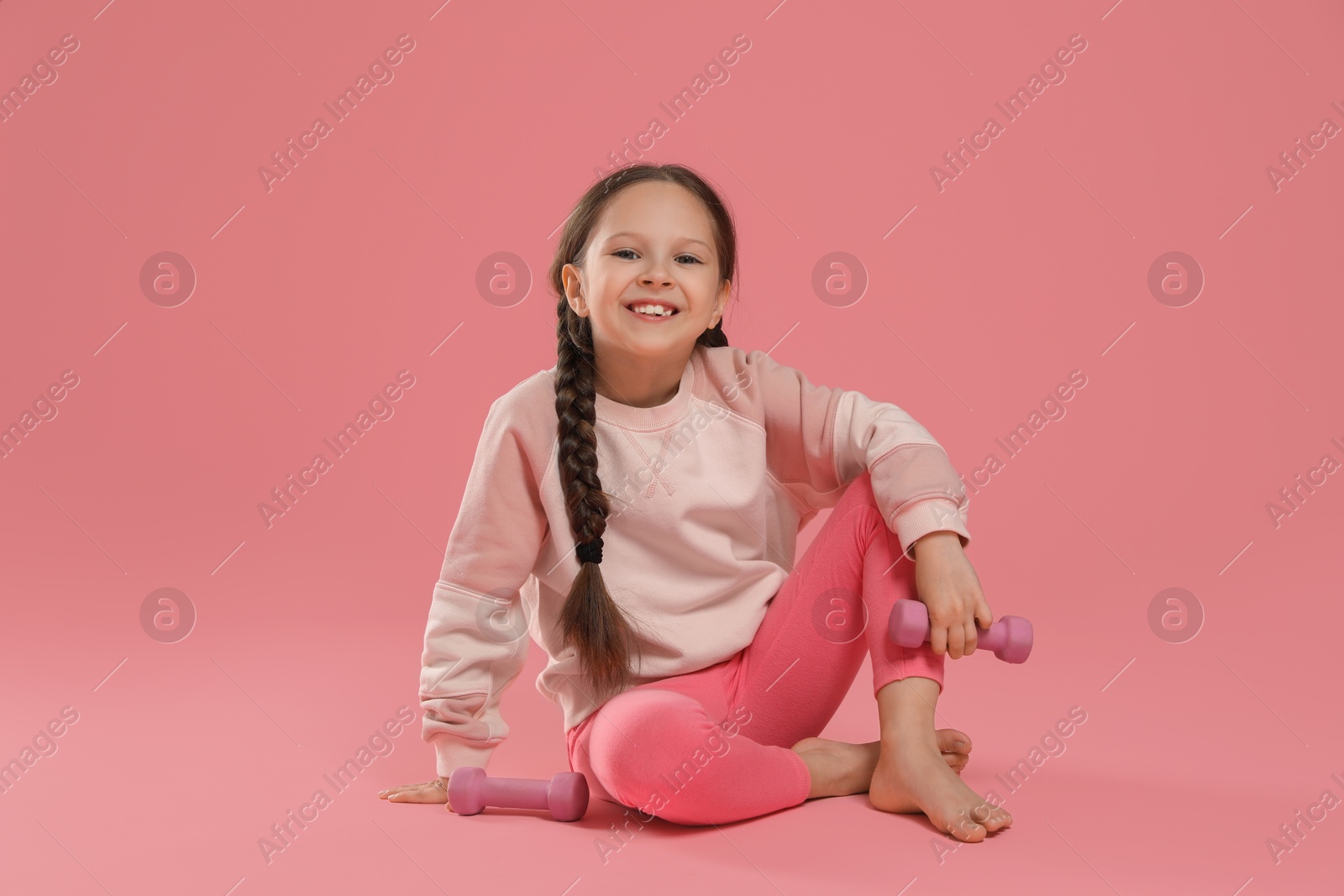 Photo of Cute little girl with dumbbells on pink background