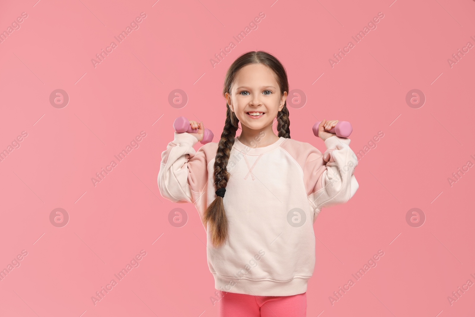 Photo of Cute little girl with dumbbells on pink background